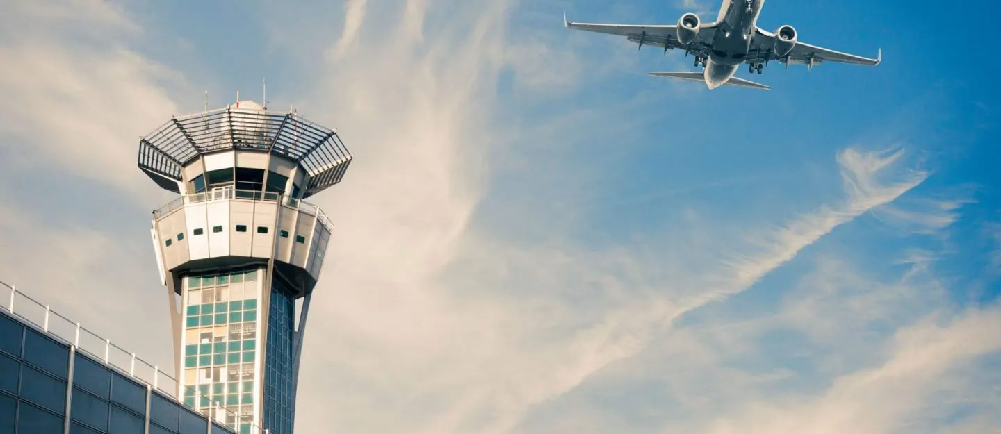 Airplane over airport and terminal with blue skies and soft clouds