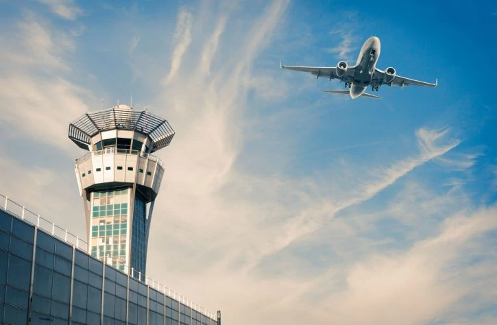 Airplane over airport and terminal with blue skies and soft clouds