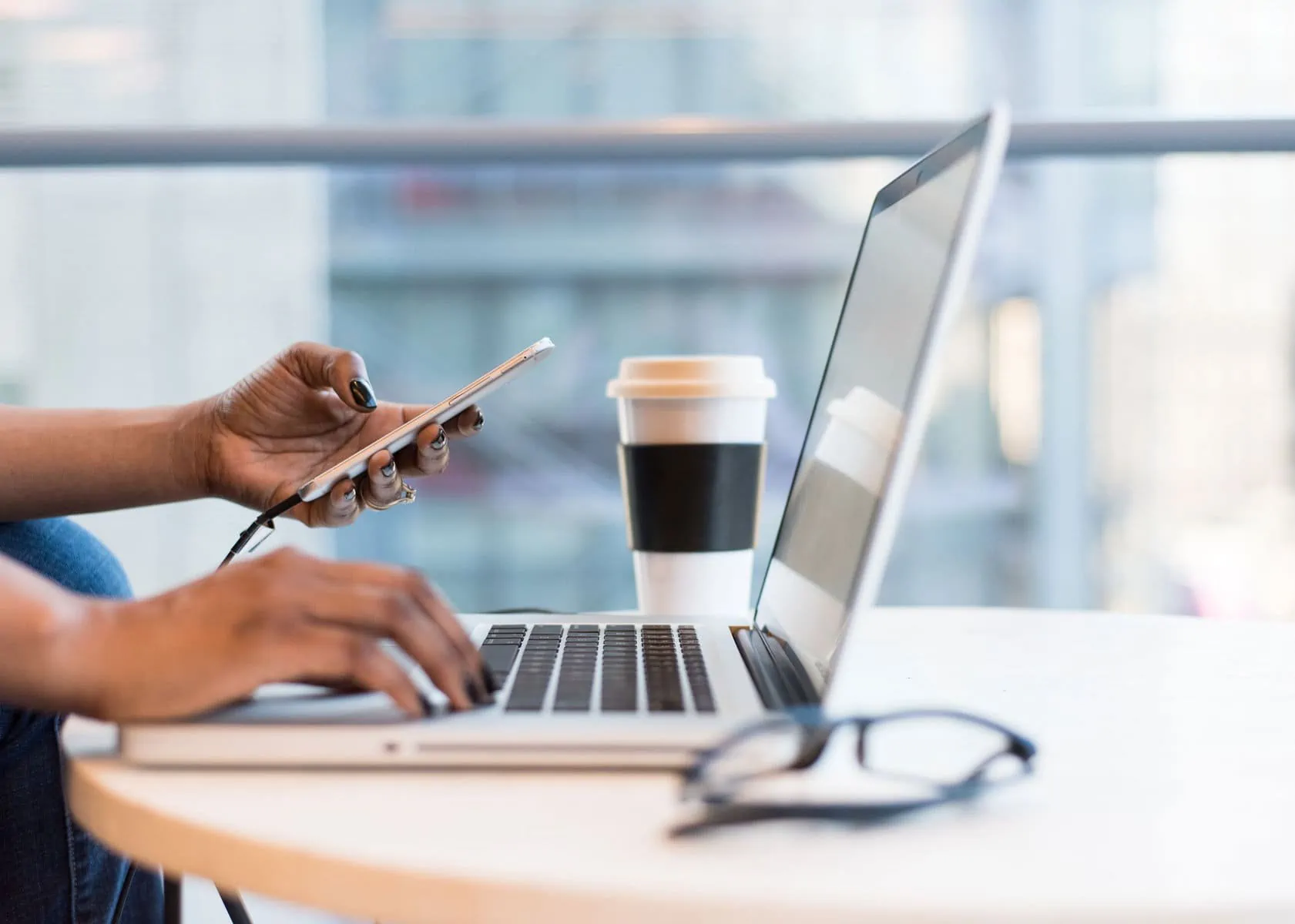 woman sits in front of a laptop and holds a smartphone in her hand